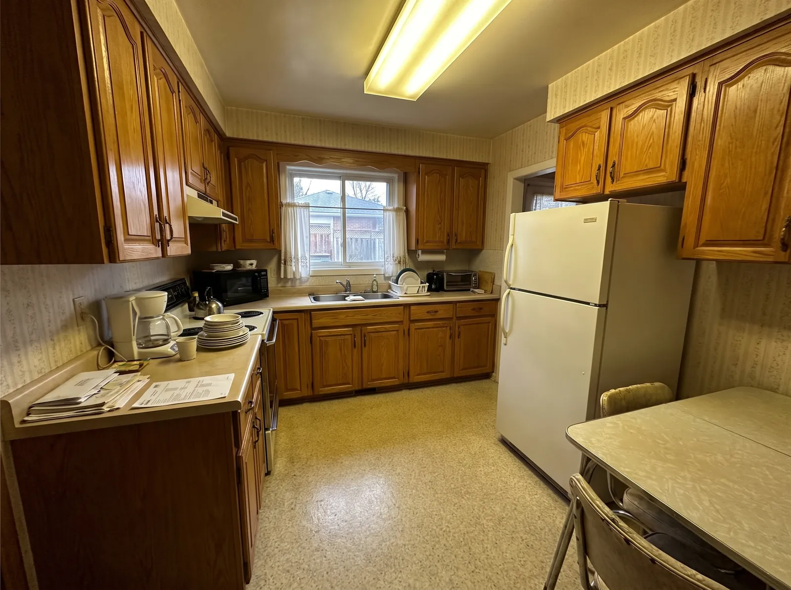 The same kitchen before renovation: a dim, cramped 1980s layout with honey-oak cabinets and dated laminate counters