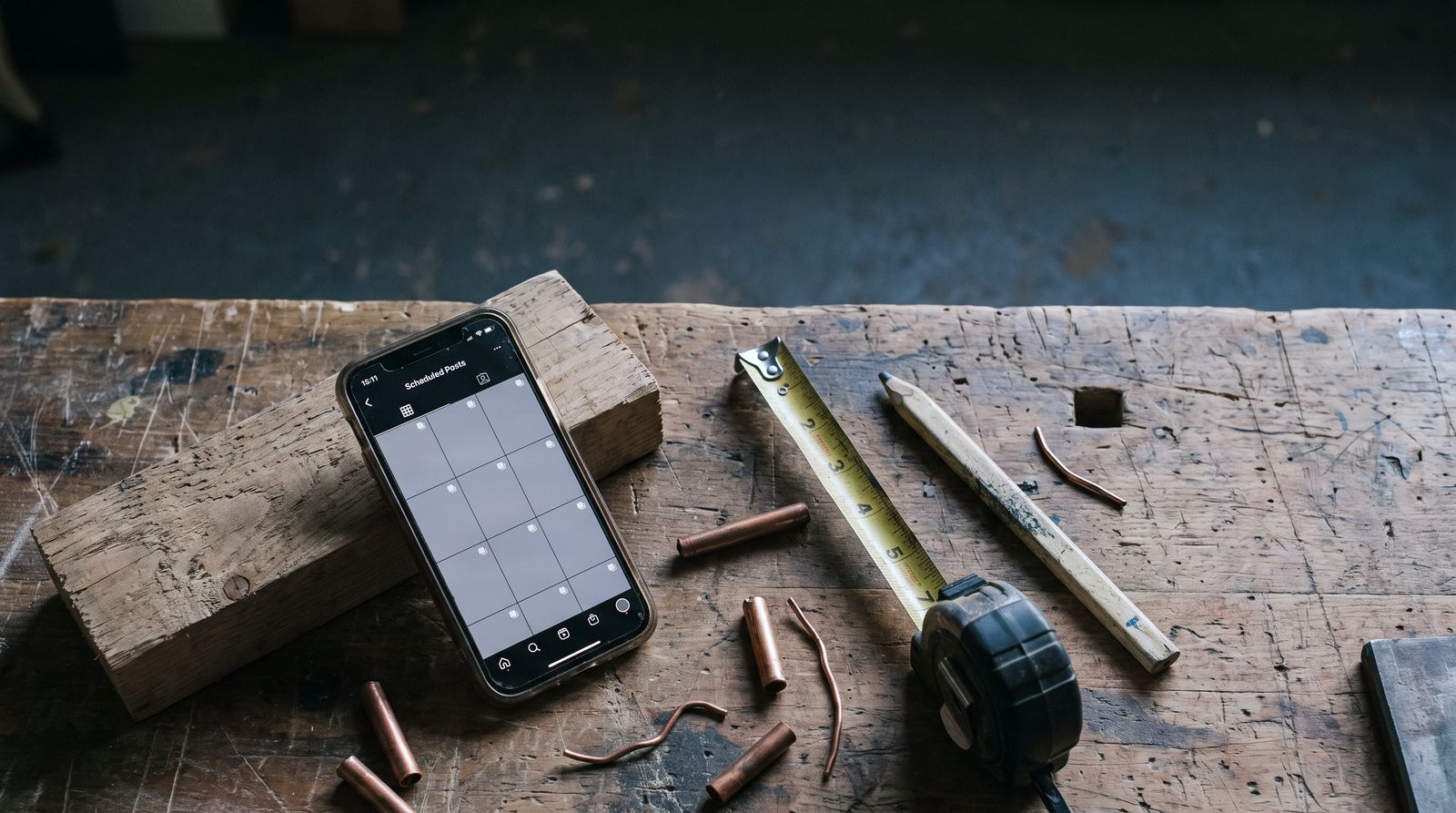 Workshop bench at the end of the day with a phone propped on a timber offcut, its screen showing a scheduled-posts view.
